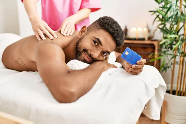 Joven Afroamericano Recibiendo Masaje Espalda Celebración Tarjeta Crédito Centro Belleza —  Fotos de Stock