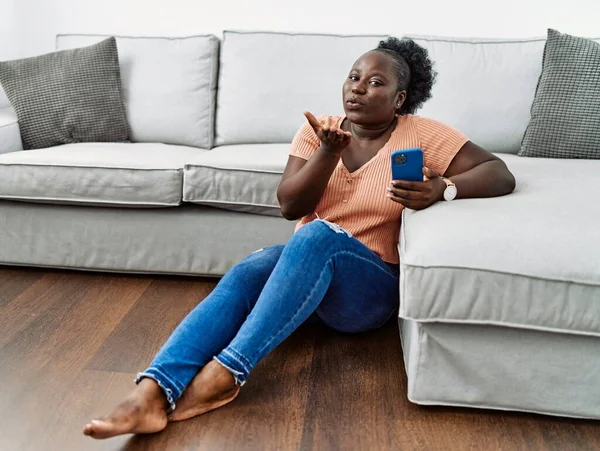 Ung Afrikansk Kvinna Använder Smartphone Sitter Golvet Hemma Tittar Kameran — Stockfoto