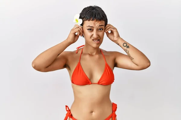 短い髪の若いヒスパニック系の女性は 大きな音楽のノイズのためにいらいら表情で指で耳をカバービキニを身に着けています 聴覚障害の概念 — ストック写真