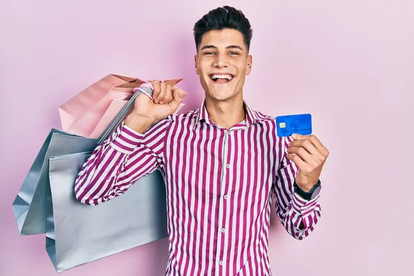 Joven Hombre Hispano Sosteniendo Bolsas Compras Tarjeta Crédito Celebrando Loco —  Fotos de Stock