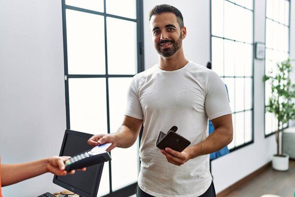 Young hispanic man customer paying purchase using credit card at clothing store