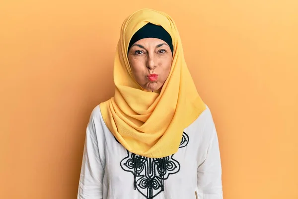 伝統的なイスラムのヒジャーブスカーフを身に着けている中世のヒスパニック女性は面白い顔で頬をむいています 口は空気で膨らみ狂気の表情で — ストック写真