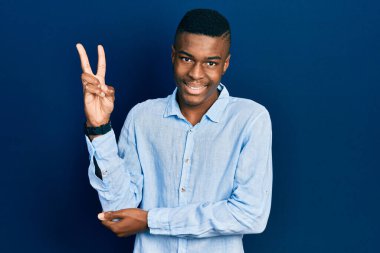 Genç Afro-Amerikalı sıradan kıyafetler giyen, gülen yüzlü, kameraya göz kırpan zafer işareti yapan genç bir adam. İki numara.. 