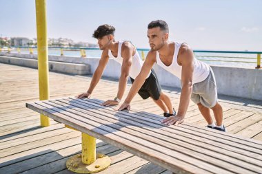 Two hispanic men couple stretching at seaside