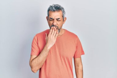 Handsome middle age man with grey hair wearing casual t shirt bored yawning tired covering mouth with hand. restless and sleepiness. 