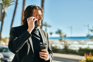 Orta yaşlı işadamı akıllı telefondan konuşuyor ve şehirde kahve içiyor..