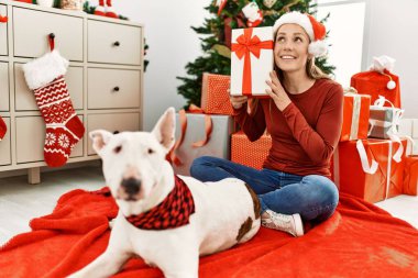 Kafkasyalı genç bir kadın elinde hediyeyle evde köpekle oturuyor.