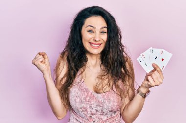 Poker kartları tutan genç İspanyol kadın gururla bağırıyor, zaferi kutluyor ve başarıyı kollarını kaldırarak kutluyor. 