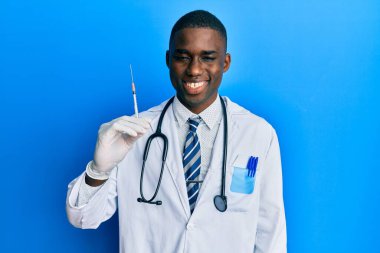 Genç Afrikalı Amerikalı doktor elinde şırınga tutarken pozitif ve mutlu görünüyor. Kendine güvenen bir gülümsemeyle dişlerini gösteriyor. 