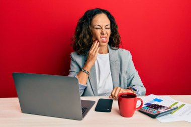Ofiste çalışan orta yaşlı güzel bir kadın diş ağrısı ya da diş ağrısı yüzünden bir fincan kahve içerek dudaklarına acı dolu bir ifadeyle dokunuyor. dişçi kavramı. 