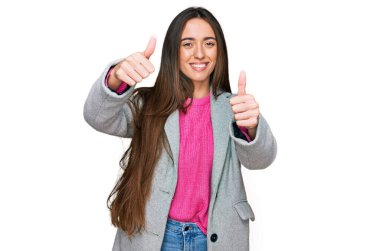 İş kıyafetleri giyen genç İspanyol kız elinle olumlu jest yapıyor, gülümsüyor ve başarı için seviniyor. kazanan jest. 