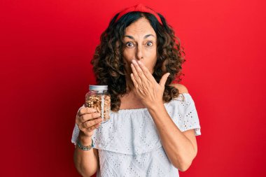 Orta yaşlı İspanyol bir kadın elinde kavanozla ağzında ceviz olan, şok olmuş ve hata yapmaktan korkan biri. şaşırmış ifade 