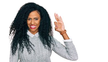 Orta yaşlı Afro-Amerikalı kadın, günlük kıyafetler giyip gülümsüyor ve el ve parmaklarıyla 