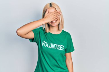 Gönüllü tişört giyen, gülümseyen ve gülümseyen güzel sarışın kadın şaşırtmak için gözlerini kapatıyor. kör kavram. 