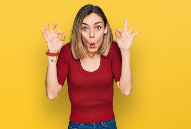 Gündelik giysiler giyen genç sarışın kız şaşırmış ve şok olmuş görünüyor tamam onay sembolünü parmaklarıyla yapıyor. çılgın ifade 