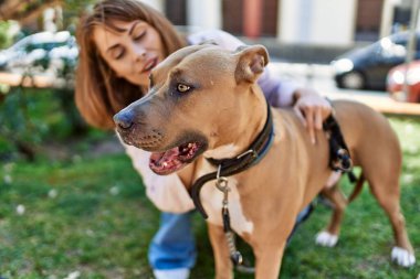 Genç beyaz kız mutlu bir şekilde gülümsüyor. Parkta köpekle duruyor..