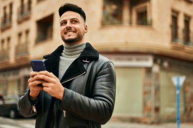 Genç Arap adam şehirde akıllı telefon kullanarak mutlu gülümsüyor..