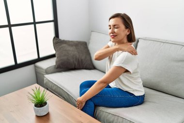 Orta yaşlı İspanyol bir kadın evinde boynu ağrıyan bir kanepede oturuyor.