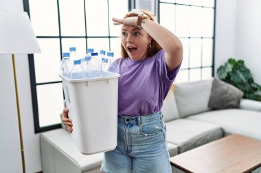 Genç kızıl saçlı kadın elinde plastik şişelerle çöpleri geri dönüşüm sepetini tutarken çok mutlu ve tebessüm ediyor. arama kavramı. 