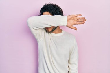 Yakışıklı, beyaz süveter giyen, kollarıyla gözlerini kapatan, ciddi ve üzgün görünen bir İspanyol. Görme, saklama ve reddetme konsepti 