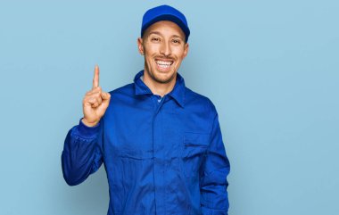 Sakallı, inşaatçı tulumu giyen kel bir adam bir numaralı parmağıyla kendini beğenmiş ve mutlu gülümserken kendini gösteriyor.. 