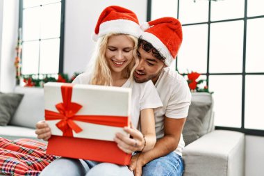 Genç çift Noel şapkası takıyor, hediyelerini açıyor ve sarılıyorlar..
