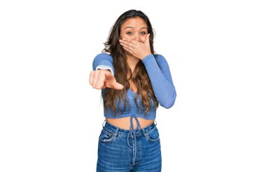 Gündelik kıyafetler giyen genç İspanyol kız sana gülüyor, eli ağzında kamerayı işaret ediyor, yüz ifadesi utanç verici. 