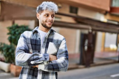 Genç İspanyol adam mutlu bir şekilde gülümsüyor şehirde çapraz hareketlerle.