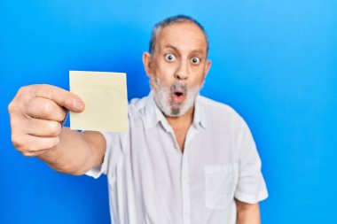 Elinde kağıt sakallı yakışıklı bir adam. Korkmuş ve ağzı açık kalmış. Şaşırmış ve şaşırmış. 