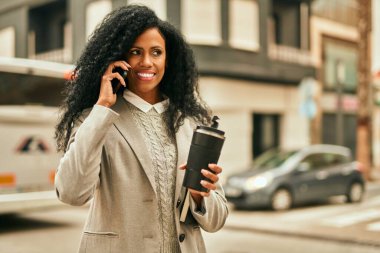 Orta yaşlı Afro-Amerikan iş kadını akıllı telefondan konuşuyor ve şehirde kahve içiyor..