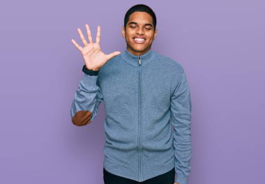 Genç, yakışıklı, sıradan bir kazak giyen, beş numaralı parmaklarını göstererek gülümseyen, kendinden emin ve mutlu bir İspanyol.. 