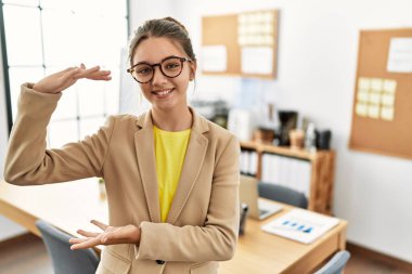 İş yerinde iş elbisesi giyen genç esmer. Elleri büyük ve büyük boy işareti, ölçü sembolü gösteren hareketler yapıyor. Kameraya bakıp gülümsüyor. ölçüm kavramı. 