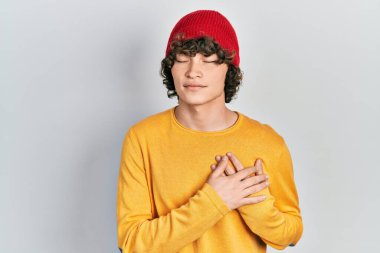 Handsome young man wearing wool hat smiling with hands on chest with closed eyes and grateful gesture on face. health concept. 