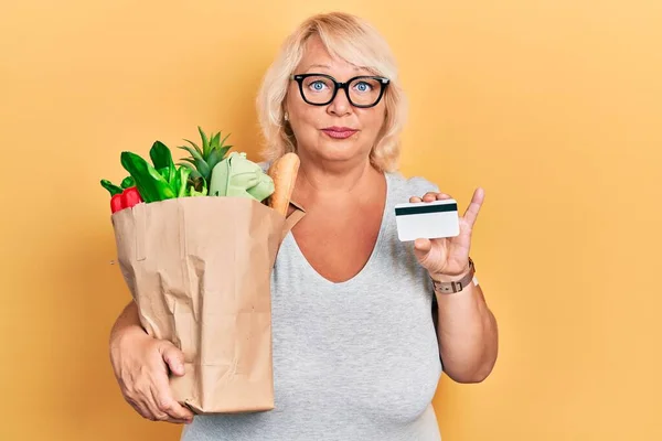 Medelålders Blond Kvinna Som Håller Matvaror Och Kreditkort Avslappnad Med — Stockfoto