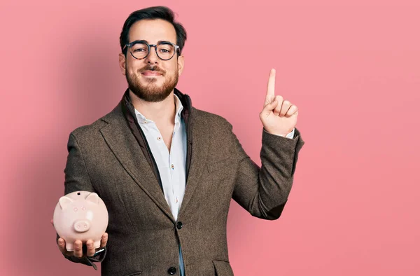 Young Hispanic Man Holding Piggy Bank Smiling Idea Question Pointing — Zdjęcie stockowe