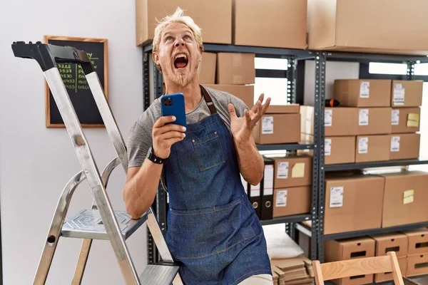 Young Blond Man Using Smartphone Working Storehouse Crazy Mad Shouting — Stock Photo, Image