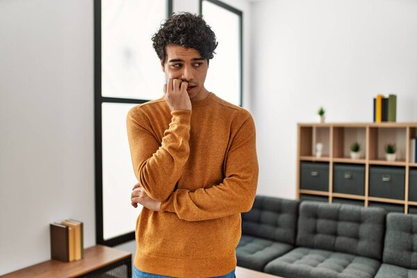 Молодой латиноамериканец в повседневной одежде, стоящий дома и выглядящий напряженным и нервным с руками на губах, грызущими ногти. тревожные проблемы. 
