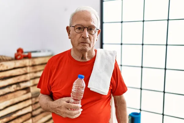 Senior man wearing sportswear and towel at the gym relaxed with serious expression on face. simple and natural looking at the camera.