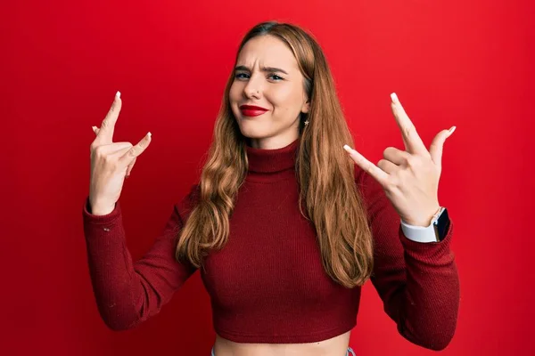 手を上げて岩のシンボルをやって狂気の表情で叫んで亀甲セーターを身に着けている若いブロンドの女性 音楽スター 重い概念は — ストック写真