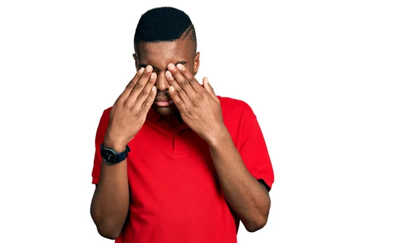 若いアフリカ系アメリカ人の男性は 疲れや頭痛 疲れた表情のために目をこすりカジュアルな赤いTシャツを着ています ビジョンの問題 — ストック写真