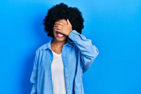 カジュアルな服を着た若いアフリカ系アメリカ人女性が笑顔で 驚きのために目を覆う顔で笑っています 視覚障害の概念 — ストック写真