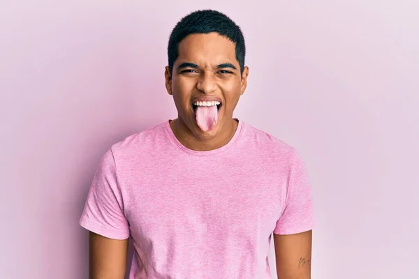 年轻英俊的他惊慌失措的男人穿着休闲的粉色T恤 带着滑稽的表情伸出舌头 情感概念 — 图库照片