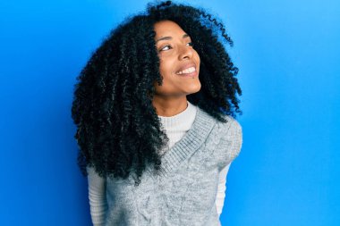 Afro saçlı, kışlık süveter giyen, yüzünde gülümseme, doğal bir ifade olan Afro-Amerikalı bir kadın. Kendinden emin gülen. 
