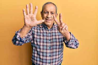 Gri saçlı yakışıklı, günlük gömlekli, yedi numaralı parmaklarıyla gösteriş yapan, kendinden emin ve mutlu gülümseyen bir adam.. 