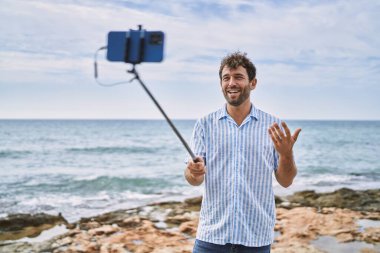 Genç İspanyol gülümseyen adam sahilde akıllı telefon kullanarak video araması yaptığı için mutlu..