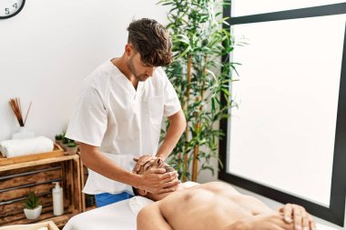 İki İspanyol erkek terapist ve hasta güzellik merkezinde yüz masajı yapıyorlar.