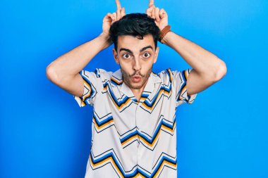 Gündelik kıyafetler giyen genç İspanyol adam boynuzlarını parmağında oynatarak komik hareketler yapıyor. 