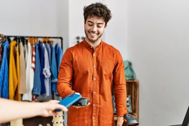 Customer hand paying to shopkeeper man using smartphone at clothing store.