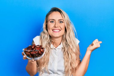 Güzel sarışın bir kadın elinde kaseyle gururla bağırıyor zaferi ve başarıyı kutluyor. 