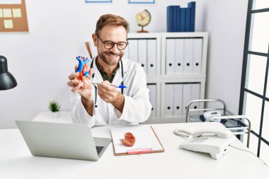 Klinikte kalbi tutan, doktor üniforması giyen orta yaşlı İspanyol bir adam.